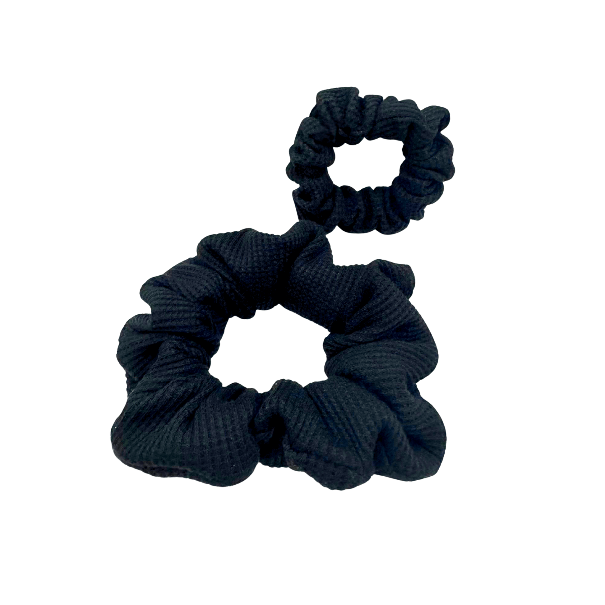 Black waffle knit cotton scrunchie with a gathered, ruffled texture, displayed against a neutral background. The ribbed fabric adds subtle dimension to the sleek black tone, offering a soft, secure hold ideal for everyday styling.
