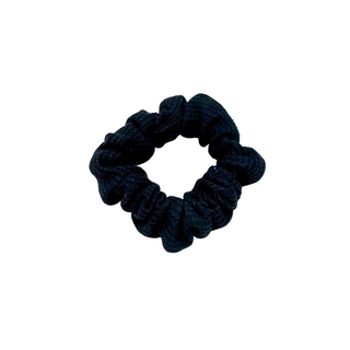 Black waffle knit cotton scrunchie with a gathered, ruffled texture, displayed against a neutral background. The ribbed fabric adds subtle dimension to the sleek black tone, offering a soft, secure hold ideal for everyday styling.