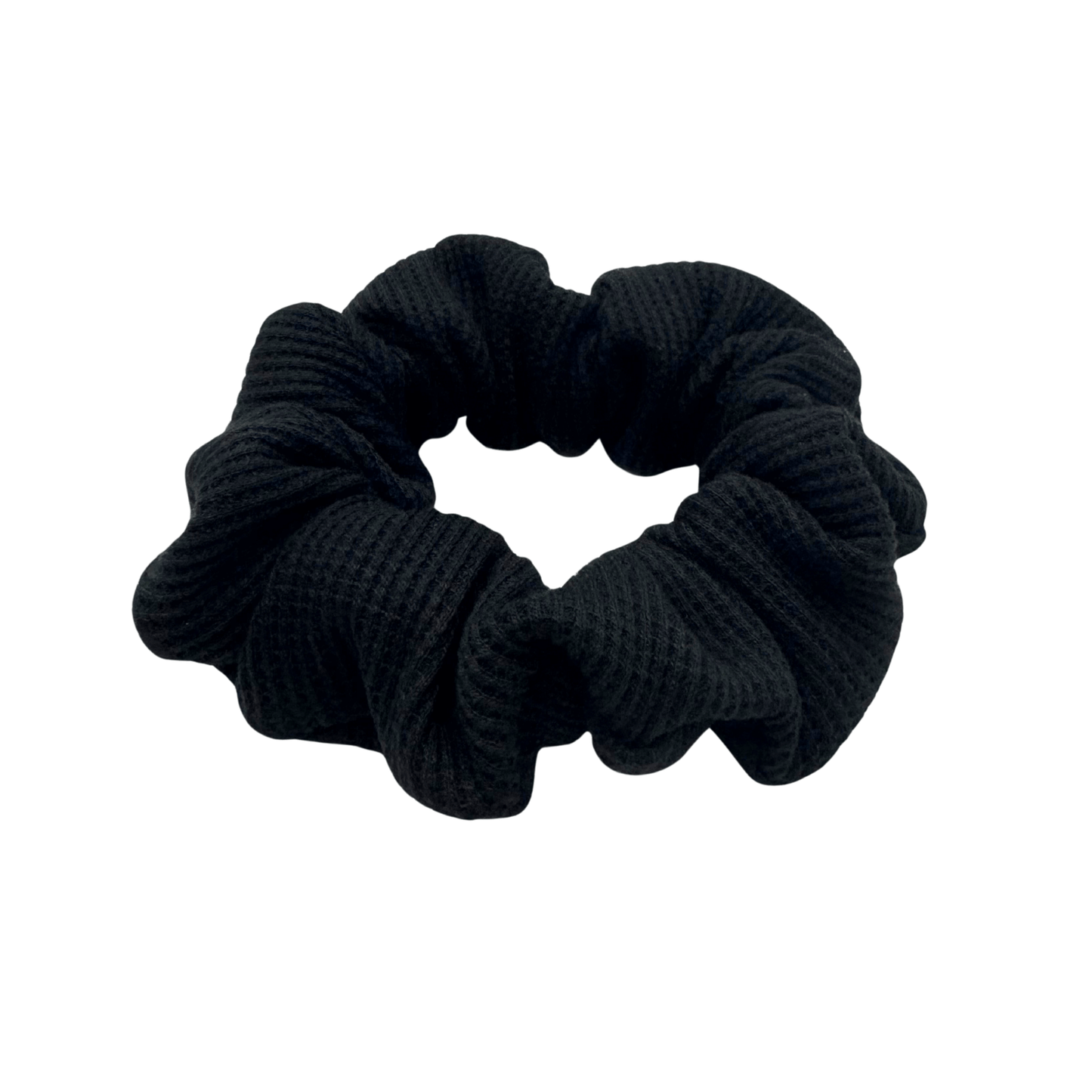 Black waffle knit cotton scrunchie with a gathered, ruffled texture, displayed against a neutral background. The ribbed fabric adds subtle dimension to the sleek black tone, offering a soft, secure hold ideal for everyday styling.